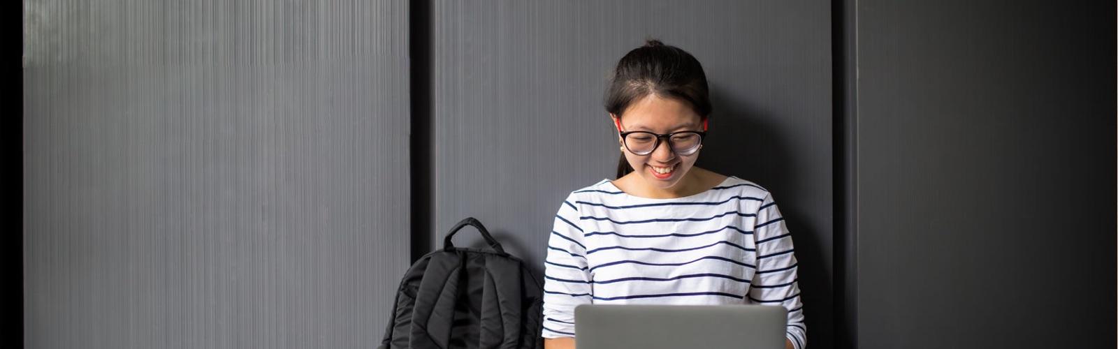 Woman sitting against a wall on her laptop