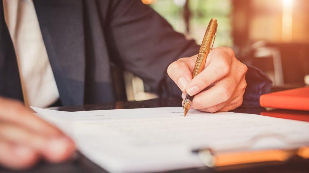 Close up of a hand writing on a piece of paper on a clipboard.